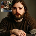 A fluffy tabby cat lounging comfortably on a blue and white blanket, with a cozy indoor background featuring folded clothes and household items, giving off a warm and relaxed vibe.
