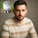 A striking cat with bright blue eyes sits attentively on green grass, framed by a rustic wooden background. The cat's detailed fur patterns and clear gaze make it the star of this natural outdoor portrait.