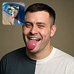 A happy dog with a gray and white coat sticks its head out of a car window, tongue playfully hanging out, enjoying the sunny day and fresh air.