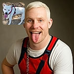 A cheerful white dog with a few brown spots is standing on a leafy ground, tongue out and looking up with bright eyes, wearing a red and black harness and a chain leash, ready for a walk or some fun outdoors.