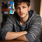 A unimpressed tabby has claimed the wooden side table as its throne, glaring at the camera with whiskers on full display while eclectic decor and a bold blue wall stage the drama.