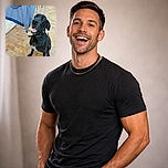 A goofy, happy black dog sits on a tiled patio with its mouth open like it's mid-conversation — a striped towel and drying rack make a domestic backdrop while the dog models a slightly askew collar and proud white chest patch.