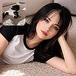 A black and white cat lounges comfortably on a fluffy beige carpet, basking in the warm sunlight streaming through a nearby window. The cat's curious yellow eyes are wide open, and its relaxed posture suggests it is enjoying a peaceful moment indoors.