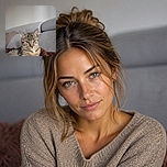 A serious tabby cat sits like the tiny landlord of the couch, gazing into the camera with the authority of someone who has just inspected the entire household. Its striped coat and bright green eyes stand out against the soft gray sofa and fluffy blanket.