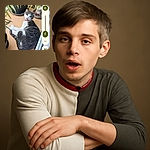 A gray and white cat with a red collar lounges on a wooden floor near some potted plants, looking back with a slightly open mouth as if caught mid-meow or mid-yawn, surrounded by a cozy indoor garden setting.