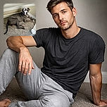 A large gray dog with a white patch on its chest is lounging comfortably on carpeted stairs, looking relaxed with one eye slightly closed as if caught mid-blink or mid-wink.