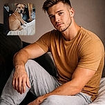 A tan and white dog is sitting on a couch looking back with a slightly concerned expression, surrounded by a cozy but cluttered indoor setting featuring wooden panel walls, a wooden chair, and various household items.
