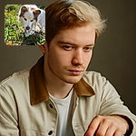 A focused close-up of a white and brown dog with piercing blue eyes, walking through a sunlit garden filled with green plants and orange flowers, looking curiously ahead with a natural outdoor backdrop.