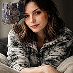 A close-up photo of a speckled dog lounging on a cozy blanket in a room filled with eclectic decorations and a clock on the wall, capturing a relaxed and intimate moment.