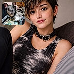 A curious dog with a speckled coat lounges comfortably on a floral bedspread, gazing intently at the camera with big, soulful eyes and ears perked up like it's ready for an adventure or a treat.