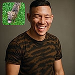 A happy brindle dog stands on a lush green clover field, looking up with a joyful expression and tongue slightly out, as if caught mid-smile during a playful moment outdoors.