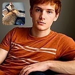 A fluffy orange tabby cat lounges on a black surface next to a glowing gaming mouse, looking curiously towards the camera with bright eyes and a soft expression. The natural light highlights the cat's fur texture and whiskers, creating a cozy and relaxed atmosphere.