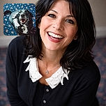 A joyful black and white dog looks up with a happy open mouth, sitting on a blue carpet patterned with pink and green floral designs, radiating pure canine delight.