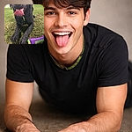 A gleeful black Labrador close-up sprawled on the grass at night, tongue lolling out like a red carpet — eyes shiny, nose glistening, and a neon purple‑green toy glowing by his paw. The scene screams joyful park-play: damp grass, distant car lights, and one very proud, slightly slobbery fetch champion.