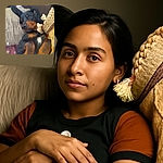 A cozy dog, possibly a Doberman or Rottweiler mix, is lying on its back among cushions and blankets, looking relaxed and slightly amused with one ear perked up like it's eavesdropping on a secret.