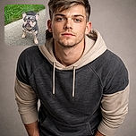 A curious little French Bulldog puppy stands on a paved path, looking up with big, soulful eyes and a slightly wrinkled face, surrounded by lush green grass and a few scattered flowers in the background.