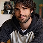 A close-up portrait of a fluffy black and brown dog with soulful eyes and a white patch on its chest, sitting indoors with a softly blurred background that highlights its expressive face and textured fur.