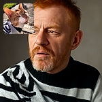 A curious orange and white cat wearing a cozy black and white sweater, basking in the sunlight with a tiny leaf resting on its head, giving it a whimsical autumn vibe.