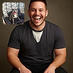 A happy, smiling dog lounges comfortably on a black cushioned swing chair indoors, with a modern white brick wall and wooden floor in the background. The dog's joyful expression and relaxed pose make it look like it's having the best day ever.