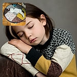 A cozy kitten is stretched out and napping peacefully on a colorful, patchwork-style round cushion, blending comfort and charm in a warm, tiled room.