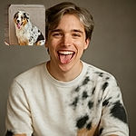 A fluffy Australian Shepherd puppy with a happy, tongue-out expression sits next to a beige couch in a cozy indoor setting. The photo is sharp and well-lit, capturing the dog's adorable spotted fur and joyful mood. The text 'Galaxy S23 Ultra' is clearly overlaid in the bottom left corner.