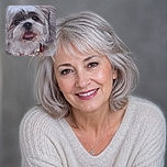 A fluffy little dog sits on a rocky surface, gazing into the camera with its tongue out like it just delivered a hilarious punchline. Its fancy fur, red collar, and tiny dangling tag give it the energy of a very shaggy celebrity caught between naps.