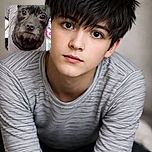 A close-up photo of a small dog wearing a striped sweater, looking curiously at the camera with big shiny eyes. The background is a colorful, fuzzy blanket adding a cozy vibe to the scene.