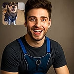 A happy dog with striking blue eyes and a playful tongue-out expression sits on a wooden floor wearing a blue and black harness, looking ready for an adventure or a treat.