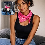 A charming black and white dog wearing a bright pink bandana sits comfortably on a blue dog bed inside a car, looking attentively out of frame with a calm and curious expression.