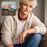 A fluffy white dog lounges comfortably on a couch next to colorful, whimsical stuffed animals, set against a backdrop of white blinds. The dog looks relaxed and slightly curious, blending perfectly with the cozy and playful vibe of the scene.