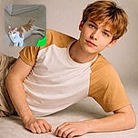 A relaxed orange and white cat lounges on a tiled floor near a corner wall, with a bright green object partially visible in the lower right corner, looking curiously at the camera with alert eyes and perked ears.