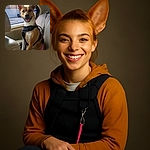 A happy dog wearing a black harness sits comfortably in the back seat of a car, tongue out and ears perked up, ready for an adventure or a car ride full of tail wags and window sniffs.