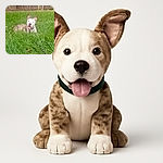 A happy dog with a brindle and white coat is lying in lush, tall green grass in a backyard, its mouth open in a joyful pant and ears perked up, with a wooden fence in the background and a leash trailing in the grass.