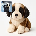 A fluffy black and white puppy is adorably sitting inside a black woven plastic basket on a tiled floor, looking curiously out with one paw draped over the basket edge, as if plotting its next playful escape.
