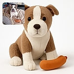 A charming dog lounges comfortably on a cozy blanket with a playful toy sausage resting near its paws, set in a home environment with a patterned quilt and colorful cushions in the background.