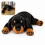 A very sleepy black-and-tan dog sprawls dramatically across the wooden floor beneath a table, looking like the household rug has finally developed paws and demanded a nap.
