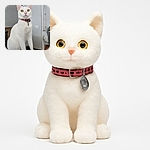 A pristine white cat with striking yellow-green eyes sits regally on a textured black surface, wearing a pink collar with a bell and tag. The background is a softly blurred indoor setting with neutral tones, highlighting the cat's elegant posture and curious gaze.
