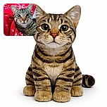 A close-up photo of a curious tabby cat wrapped in a cozy red blanket decorated with white snowflakes, staring intently at the camera with big, shiny eyes.
