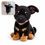 A curious little black and tan puppy with oversized ears is stepping forward on a tiled floor, its face close to the camera making its features appear adorably distorted and slightly blurry. The background shows metal chair legs and a wooden panel, giving a cozy indoor vibe.