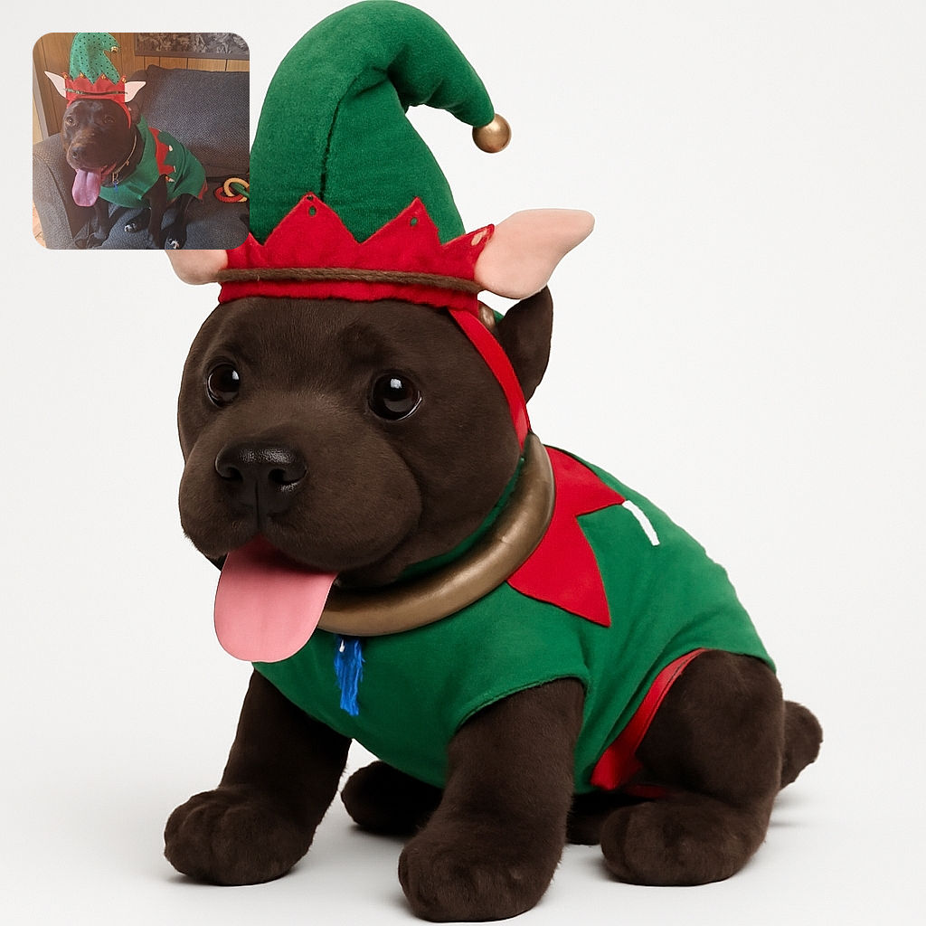 A happy black dog wearing a festive green and red elf costume sits on a gray couch with its tongue hanging out, looking ready to spread holiday cheer. The cozy wooden wall and colorful toys in the background complete the warm, cheerful scene.