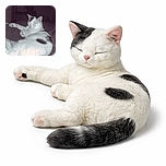 A relaxed white and black cat is lounging comfortably on a bed with its eyes closed, looking like it's in a deep, peaceful nap. The dimly lit room in the background adds a cozy, quiet atmosphere.