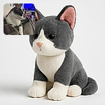 A cozy gray and white cat lounges comfortably on a soft, textured blanket, gazing thoughtfully to the side. The background reveals a cozy living room with a vibrant blue TV screen and a red flower pot adding a splash of color.