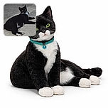 A sleek black and white cat lounges on a tiled floor, looking curiously at the camera with bright yellow eyes and a blue collar, surrounded by a simple, dimly lit background.