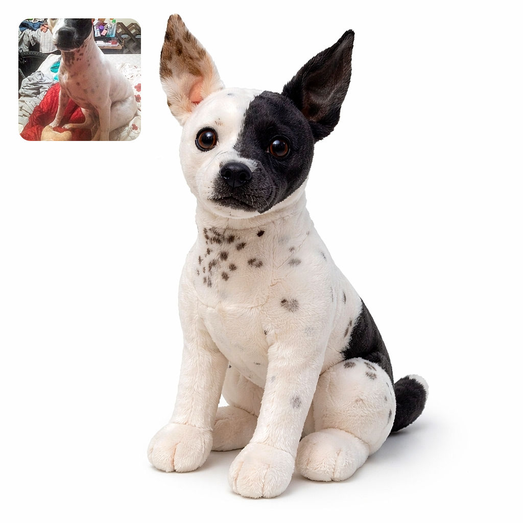 A spotted dog with one black and one white ear sits attentively on a bed covered with a red and white floral blanket, next to a plush toy that looks like a dog. The background is cluttered with clothes and household items, giving a cozy, lived-in vibe.