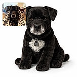 A dignified black dog wrapped snugly in a cozy white blanket adorned with playful bone and paw prints, sitting comfortably on a couch with a softly blurred living room background featuring a fireplace and shelves.