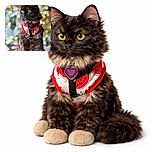 A fluffy tortoiseshell cat wearing a cute watermelon-themed harness poses regally against a dreamy bokeh background of warm yellow and white lights, looking off to the side with bright, curious eyes.