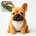 A charming French Bulldog sits on a strip of artificial grass next to a concrete path, looking slightly grumpy but adorable with its tongue peeking out. The background features a beige fabric screen providing a neutral backdrop that highlights the dog's expressive face.