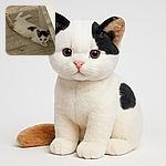 A small kitten with white fur and black spots is lying on a wooden floor, peeking out from behind a piece of furniture with curious wide eyes, ready to pounce or nap.