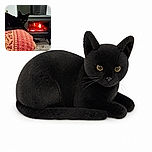 A sleek black cat lounges like a tiny panther on a richly patterned blanket, giving the camera a serious stare while a glowing wood stove crackles behind it. The cat clearly considers itself the official supervisor of cozy winter evenings.