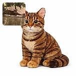 A tabby cat lounges comfortably on a white tree skirt under a festively decorated Christmas tree adorned with glowing lights and ornaments, next to a clear ball filled with colorful yarn, creating a cozy holiday scene.